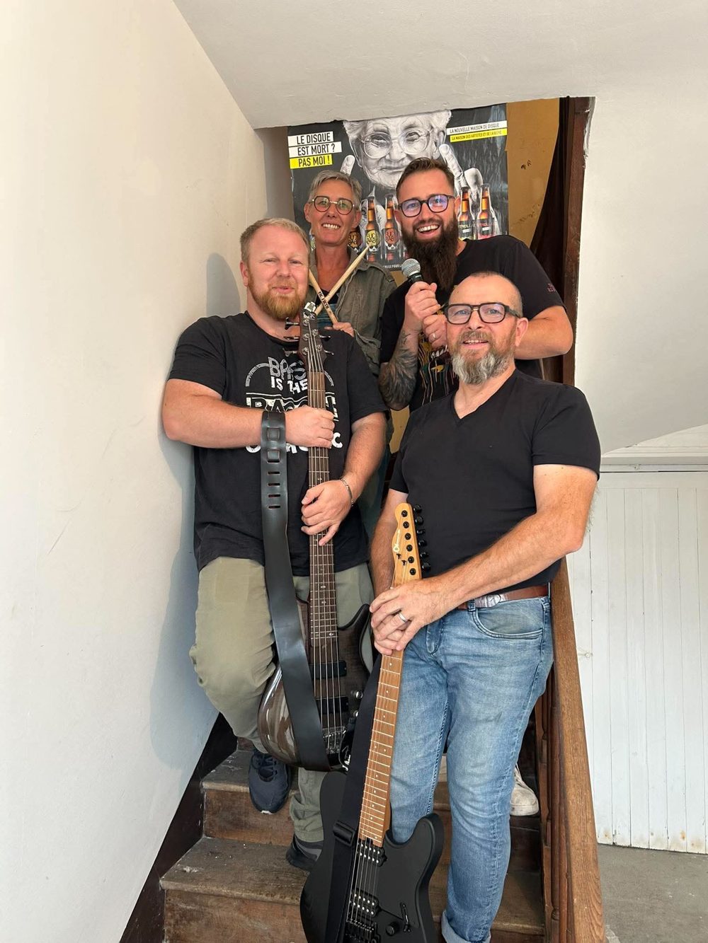 Les quatre membres de K7 dans un escalier, avec basse, guitare, micro et baguettes